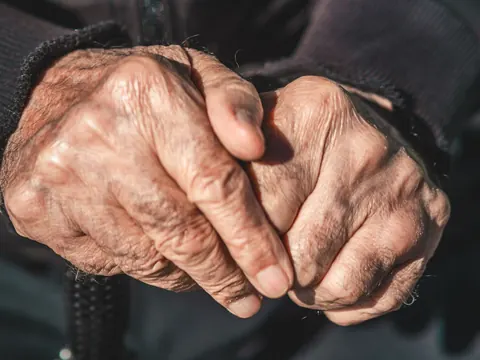 Older hands clasped in pain