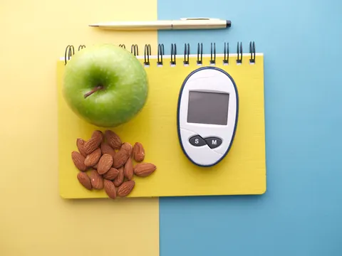 A blood sugar meter beside an apple and almonds
