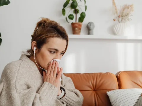 A woman with a cold blowing her nose on the sofa