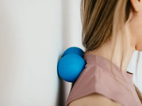 A woman easing neck pain with a massage ball against the wall