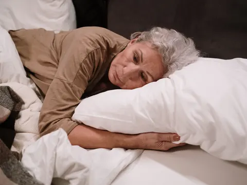 An older woman lying in bed, hugging her pillow