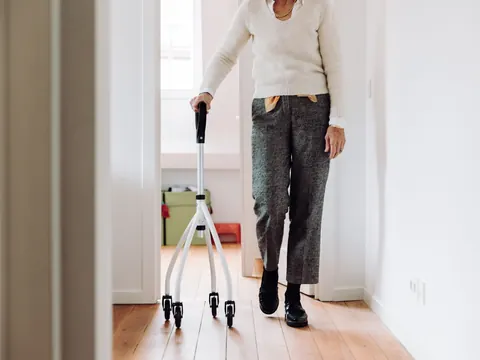An older woman walking down her hallway with a quad cane