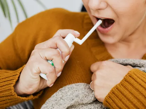 A woman with a sore throat using a throat spray