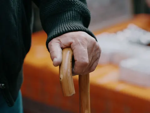 An older hand resting on a walking cane
