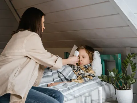 A mother taking her son's temperature in his bed