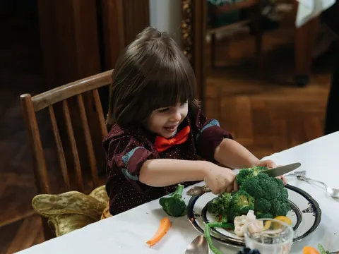 A child cutting broccoli at the dinner table