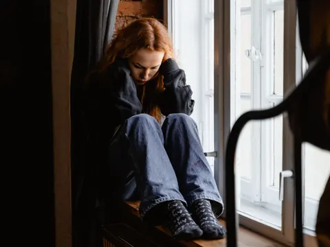 A young woman by the window, head in her hands