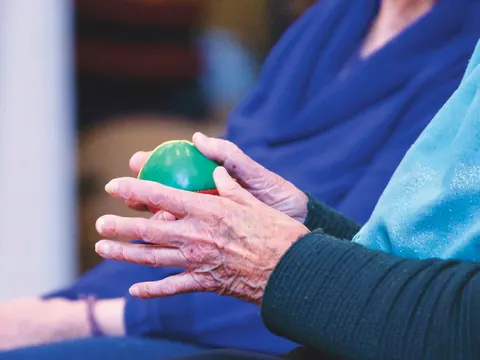 Older hands with arthritis squeezing an exercise ball