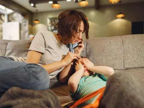 A mother on the phone, her child lying on the sofa