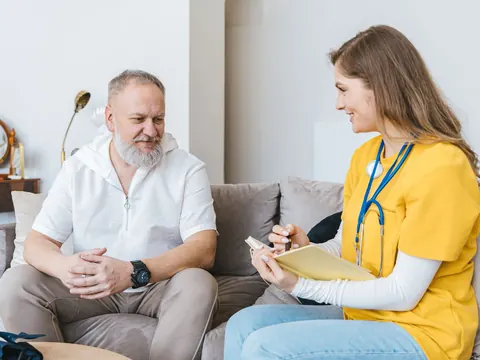 A health visitor talking with an older man on his sofa at home