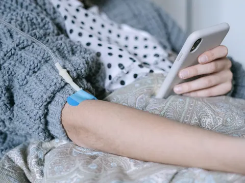 An IV drip line taped to a patient’s arm, in bed at home